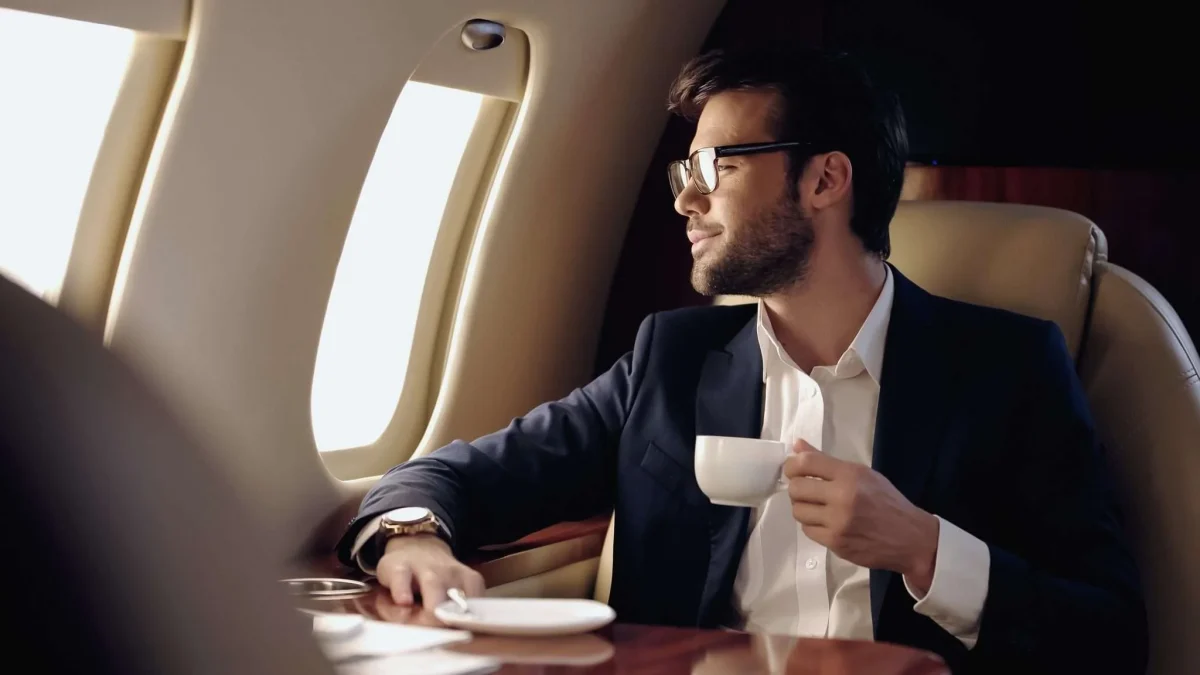 man happily looking out of aeroplane window while drinking a coffee