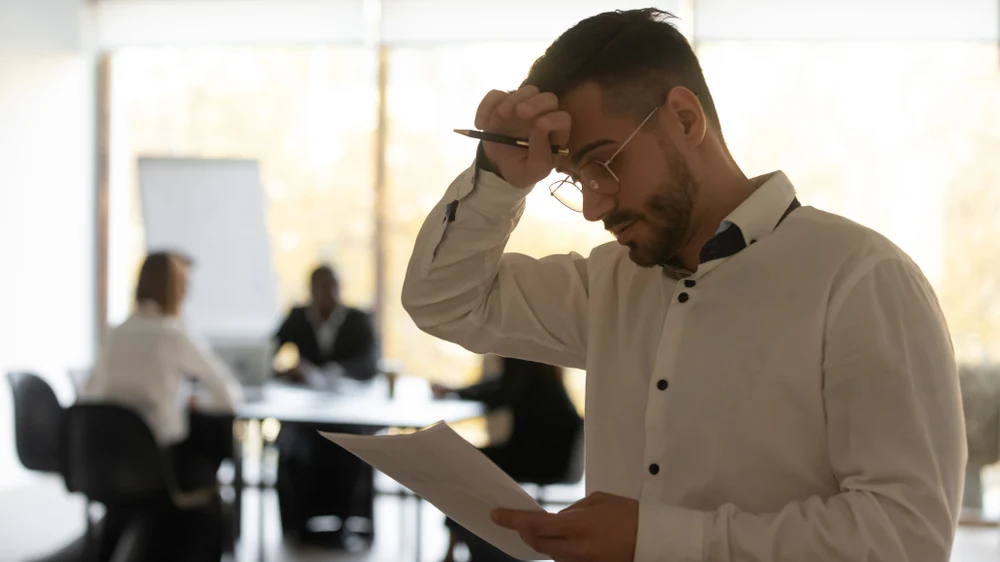 A man, wiping his brow because he is dealing with alcohol sweats whilst at work - the effects and risks of alcohol addiction.